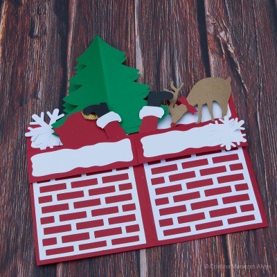 Cartão de Natal com chaminé, árvore e figuras de Papai Noel e veados em papel colorido