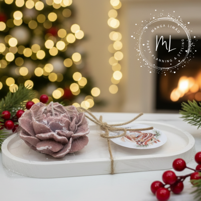 Vela rosa em forma de flor sobre base branca com cartão natalício e ramos de frutos vermelhos.