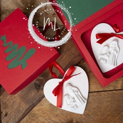 Ornamentos de Natal brancos em forma de coração com figuras da Sagrada Família, em caixas vermelhas com árvore de Natal verde.