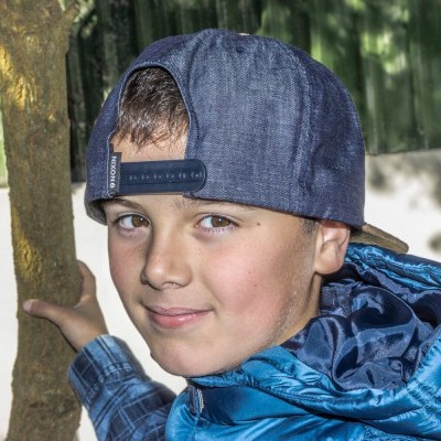 Menino com casaco azul e boné de ganga segurando tronco de árvore em jardim