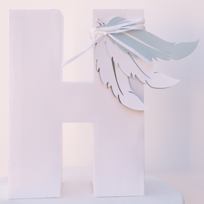 Letra decorativa 'H' branca com penas cinzentas amarradas no topo