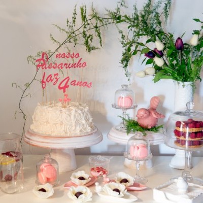 Mesa com bolo branco, decoração floral natural, doces rosa e jarra de chá com limão e framboesas