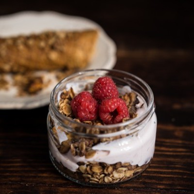 Frasco de vidro com iogurte, granola e framboesas frescas no topo