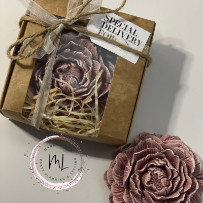 Caixa de presente castanha com etiqueta SPECIAL DELIVERY, flor decorativa roxa e palha dentro, flor semelhante fora da caixa e selo circular de marca.