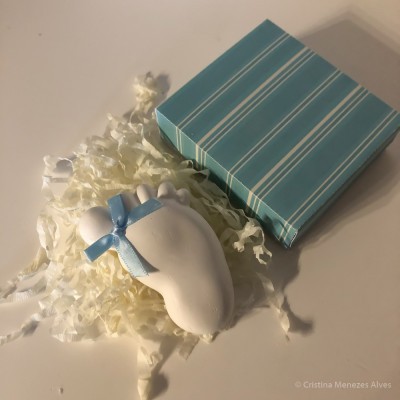 Escultura de pé de bebé branco com laço azul ao lado de caixa azul às riscas