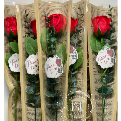 Cinco rosas vermelhas artificiais embaladas em plástico com etiqueta Para ti e folhas verdes.