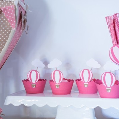 Decoração com suportes de cupcakes rosa e balões aerostáticos cor de rosa e branco em suporte branco