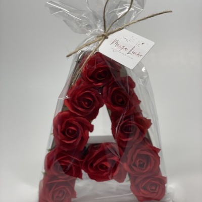 Arranjo decorativo em forma da letra A com flores vermelhas embalado em plástico transparente