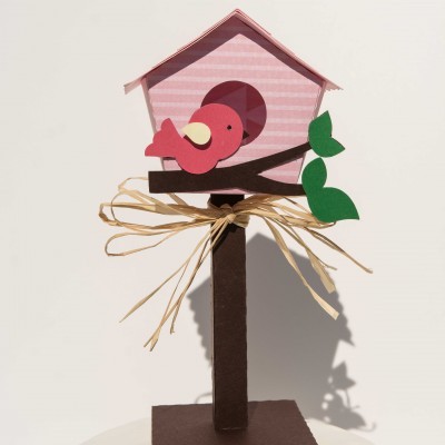 Casa de pássaro decorativa em cores rosa, vermelho e castanho em suporte com laço