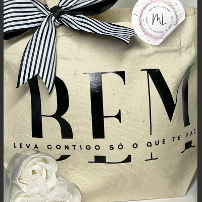 Saco de pano com laço preto e branco, etiqueta redonda e recipiente em forma de coração com rosas brancas.