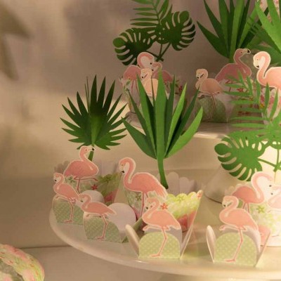 Doces decorados com folhas verdes e flamingos cor-de-rosa sobre suportes brancos.