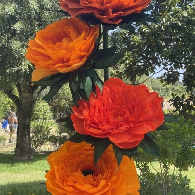 Flores artificiais grandes laranja em suporte verde num jardim