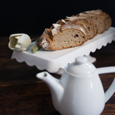 Fatias de pão rústico em travessa branca com flor e chaleira branca