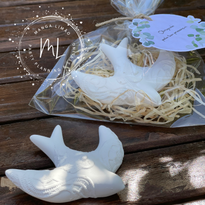 Sabonetes brancos em forma de pássaro com embalagem e etiqueta decorativa sobre madeira