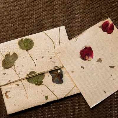 Dois cadernos artesanais com folhas e flores secas na capa sobre tecido castanho