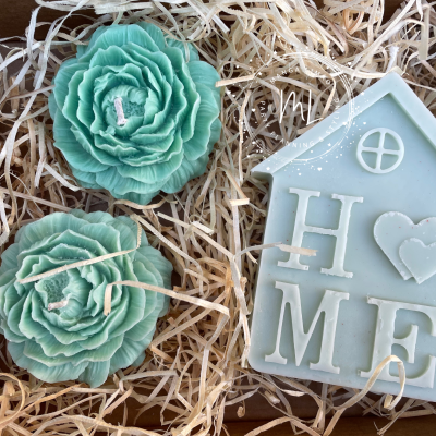 Velas verdes em forma de flores e placa de parafina em forma de casa com a palavra HOME sobre cama de palha.