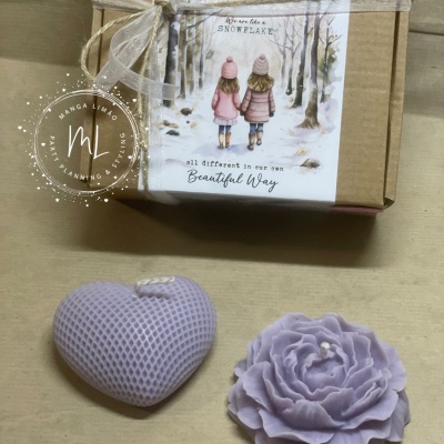 Caixa com ilustração e vela em forma de coração lilás ao lado de flor lilás decorativa.