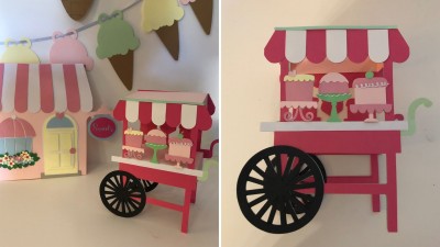 Carrinho decorativo rosa e vermelho com roda preta grande e bolos em miniatura