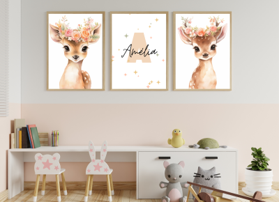 Três quadros com veados e nome Amélia pendurados numa parede sobre mobília branca com brinquedos e cadeiras pequenas.