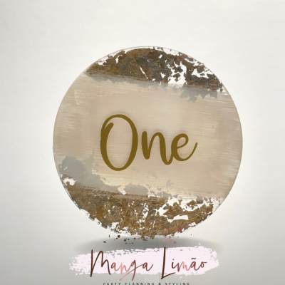 Produto decorativo redondo com a palavra One em dourado e detalhes metálicos