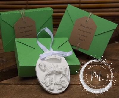 Embalagens verdes com etiquetas castanhas e decoração branca em relevo com laço, sobre superfície de madeira