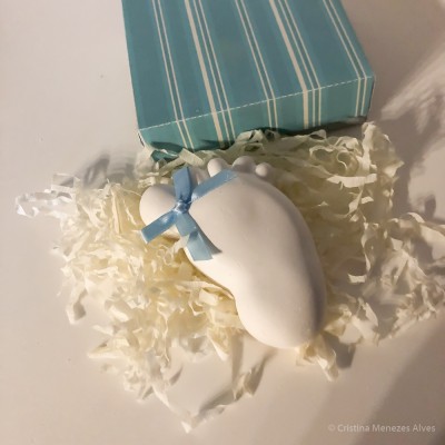 Sabonete em forma de pé de bebé com laço azul ao lado de caixa azul às riscas.