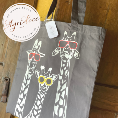 Saco de pano cinza com desenho de três girafas usando óculos coloridos