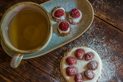 Chávena azul com chá verde e bolachas com framboesas sobre mesa de madeira