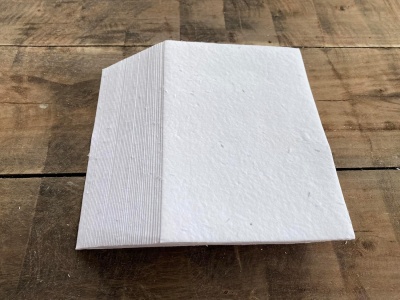 Pilha de folhas de papel branco texturizado com padrão de linhas finas na lateral sobre mesa de madeira