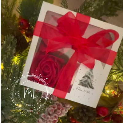 Caixa branca com rosa vermelha, fita vermelha e etiqueta FELIZ NATAL