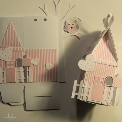 Casinha de papel rosa com padrões de riscas e corações, incluindo uma coruja de papel pequena