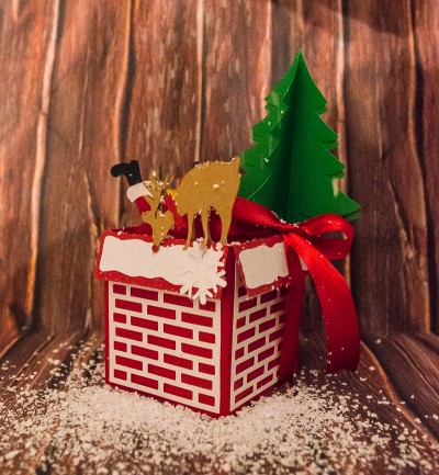 Caixa decorativa natalícia com rena dourada e árvore verde sobre fundo de madeira