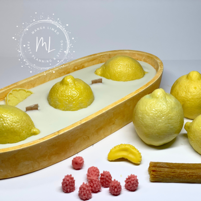 Vela decorativa em forma de limão numa base oval com limões reais e pequenos objetos decorativos ao redor