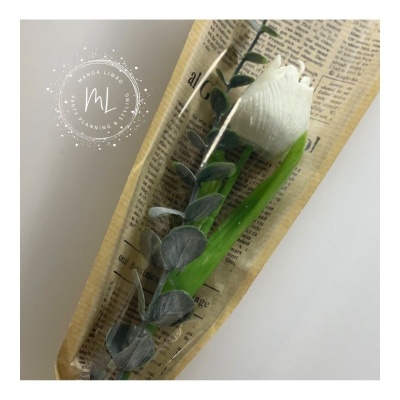 Flor branca artificial embrulhada em papel estilo jornal com folhas verdes artificiais