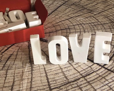 Letras brancas cerâmicas formando a palavra LOVE com embalagem vermelha sobre superfície imitando tronco