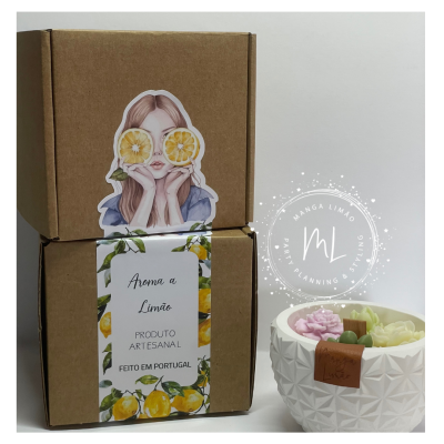 Caixas de cartão com etiquetas decorativas e vela num recipiente branco com flores cor-de-rosa e verde.