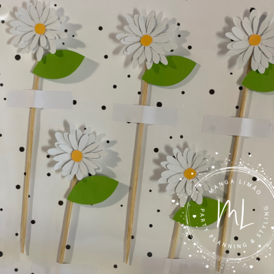 Espetos decorativos com flores de papel branca e amarelas sobre fundo branco com pontos pretos.