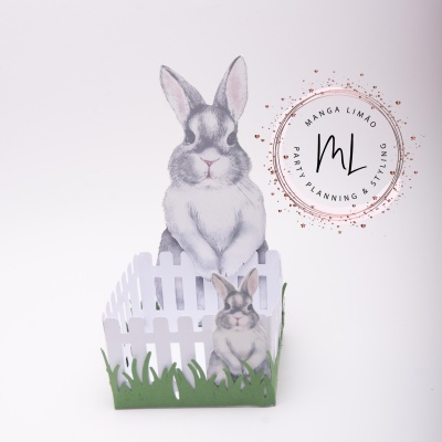 Decoração em papel com coelhos e cerca branca com relva verde junto a selo decorativo