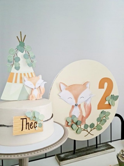 Bolo branco decorado com raposa e placa de madeira com nome Theo, painel com raposa e número 2