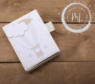 Caixa branca com ilustração de balão de ar quente em tons claros sobre madeira.