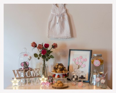 Conjunto decorativo com vestido branco, flores, quadro, bebidas, bolos, letras de madeira e luzes em aparador