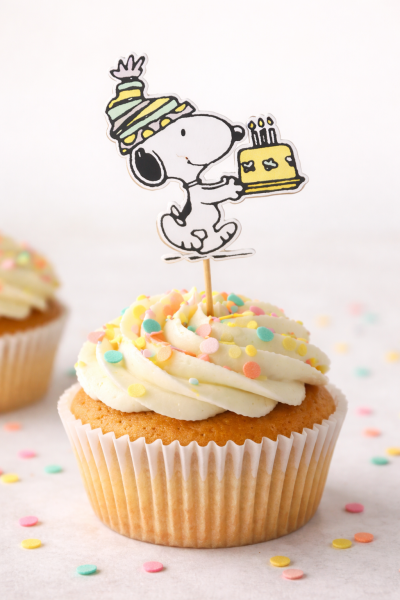Cupcake com cobertura branca, confeitos coloridos e topper do Snoopy com bolo amarelo
