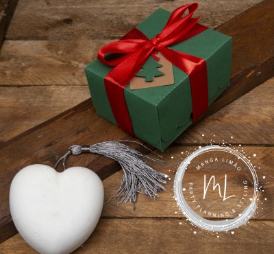 Caixa de presente verde com fita vermelha e ornamento em forma de coração branco com borla cinza