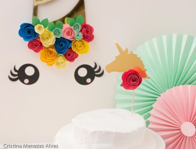 Bolo branco com decoração de unicórnio e flores de papel coloridas na parede