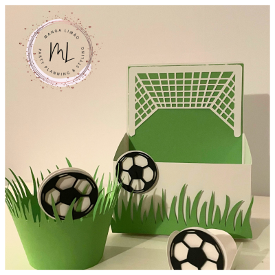 Decoração de festa com tema futebol incluindo suporte de papel verde, balde branco com relva e baliza, bolas de futebol como enfeites.