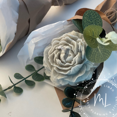 Arranjo floral artificial com flor cremosa e folhas verdes em embalagem de papel castanho e celofane branco