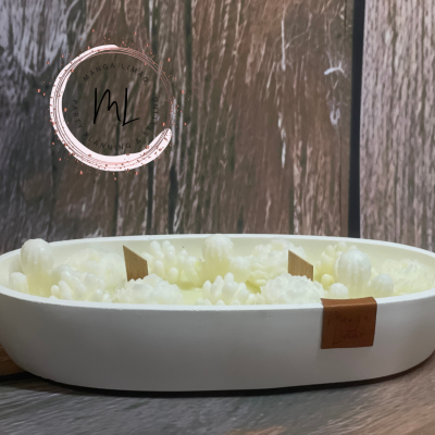 Vela branca decorativa em recipiente oval com textura de frutos sobre superfície madeira escura