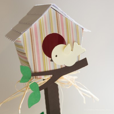 Casa de passarinho decorativa listrada com pássaro amarelo e folhas verdes