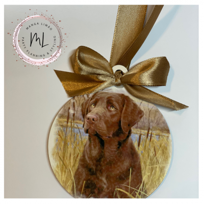 Ornamento redondo com um cão castanho numa paisagem campestre e fita dourada
