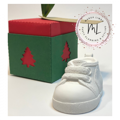 Caixa de presente verde e vermelha com sapatinho de bebé branco em tecido e borracha